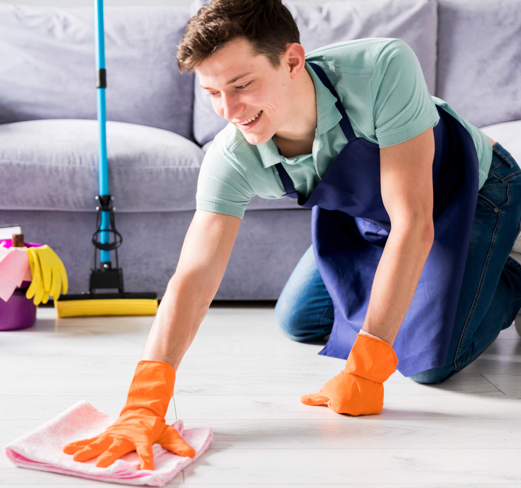 A man cleaning a living room floor with orange gloves.