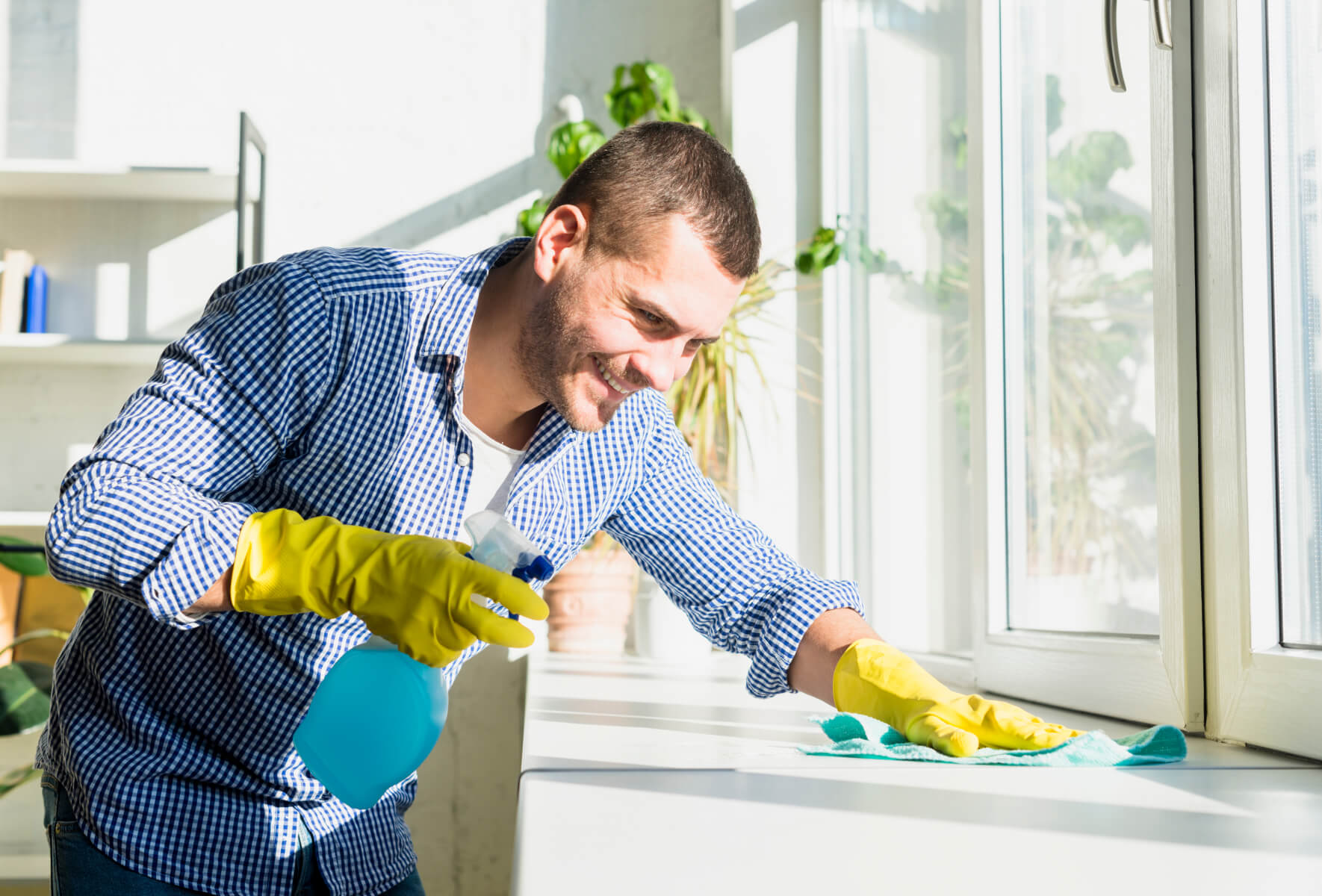 A man in a blue shirt and yellow gloves cleaning a window.